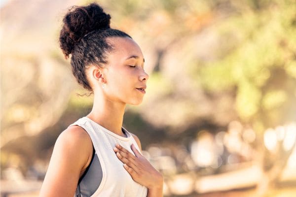 Donna con gli occhi chiusi e mano sul petto a simboleggiare come la respirazione modifica l'HRV e il cuore