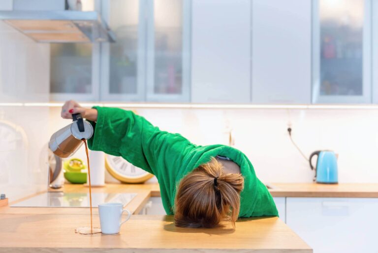 Donna esausta con la testa appoggiata sl tavolo mentre versa il caffè fuori dalla tazza