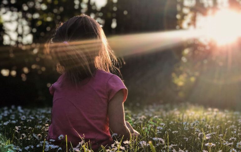 Donna seduta nel prato con la luce del sole che le accarezza il viso a simbolo del corso Spegni la Lavatrice mentale